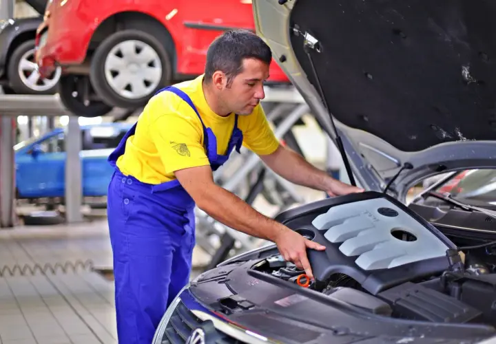 Mechanik w żółtej koszulce i niebieskich ogrodniczkach sprawdza silnik. Zastanawiasz się, ile zarabia kierowca mechanik?