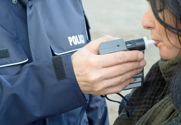 Policjant w mundurze z napisem "POLICJA" trzyma alkomat, a kobieta dmucha w jego ustnik. To przykład, jak dmuchać w alkomat.