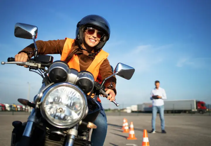 Uśmiechnięta kursantka na motorze, w kamizelce odblaskowej i kasku, uczy się jeździć. Zastanawiasz się, ile kosztuje prawo jazdy na motor?