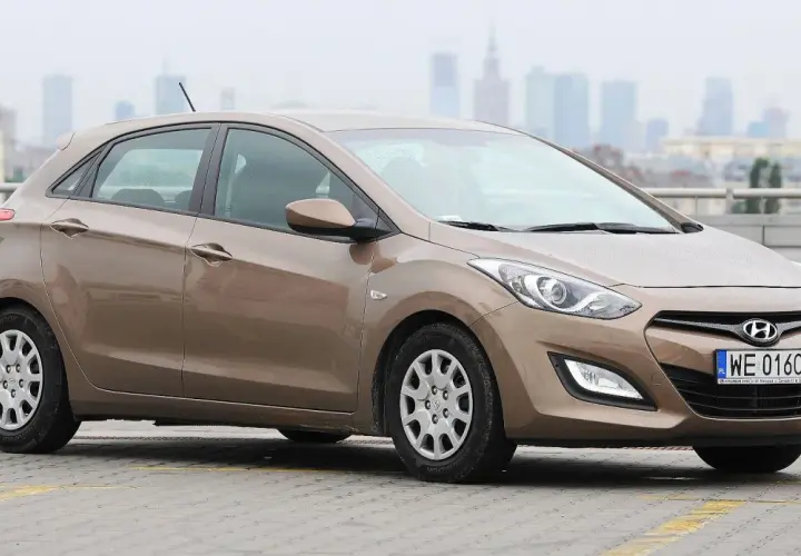 Brązowy Hyundai i30 1.4 benzyna na parkingu, w tle miejska panorama.