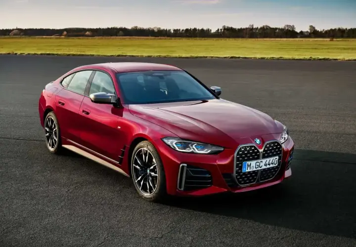 Czerwone BMW Gran Coupe na tle zielonych pól i błękitnego nieba. Elegancka linia nadwozia i sportowe felgi podkreślają dynamiczny charakter tego auta.