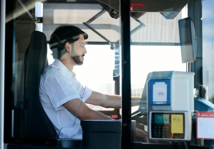Mężczyzna za kierownicą autobusu, zastanawiający się, ile zarabia kierowca autobusu. Widoczny biletomat i siedzenie kierowcy.