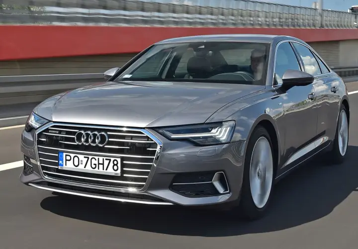 Szary sedan Audi A6 jedzie po drodze, widoczny przód i bok.
