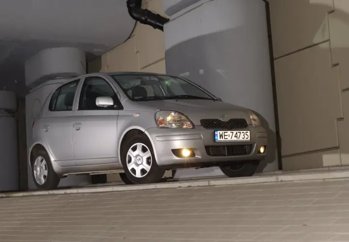 Srebrny Toyota Yaris 1.4 D4D, z tablicą WE 74735, zaparkowany pod betonowym zadaszeniem.