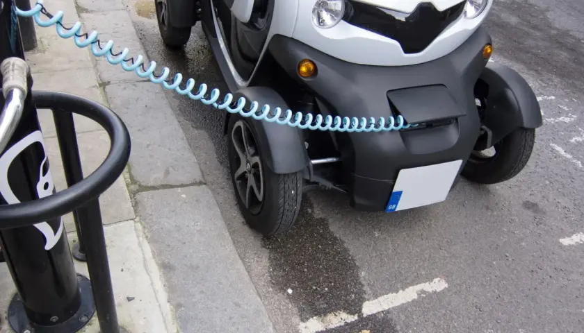 Mały, biały pojazd elektryczny z niebieskim kablem zabezpieczającym. Czy smartem można jeździć bez prawa jazdy? To zależy od modelu i przepisów.