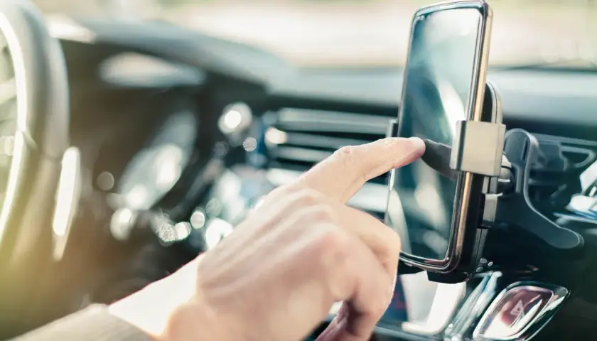 Palec dotyka ekranu telefonu w uchwycie. To **przerwa w OC, jak uniknąć kary** – sprawdź, czy masz ważne ubezpieczenie przed podróżą.
