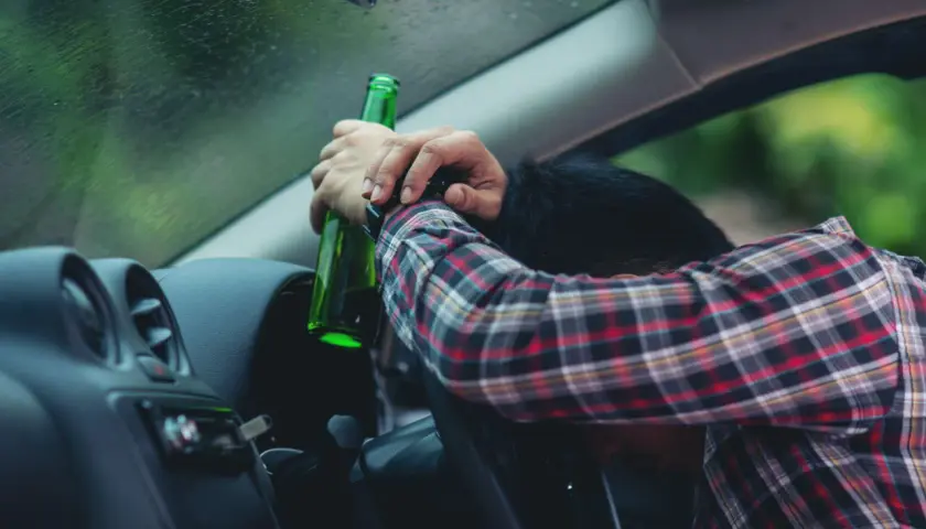 Pijany kierowca z butelką piwa w ręku. Za alkohol 1 promil prawo jazdy zabierają.
