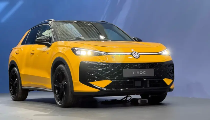 Żółty Volkswagen T-Roc z czarnym dachem i felgami. Zbliżenie na przód auta, widoczne światła LED i atrapa chłodnicy.