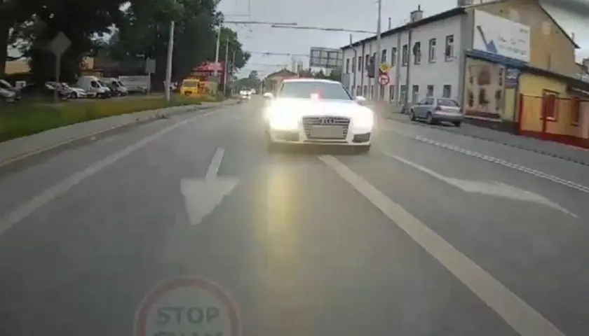 Białe Audi S7 z włączonymi światłami i sygnałem świetlnym jedzie ulicą. Kierowca tego auta prawdopodobnie spieszy się na interwencję.