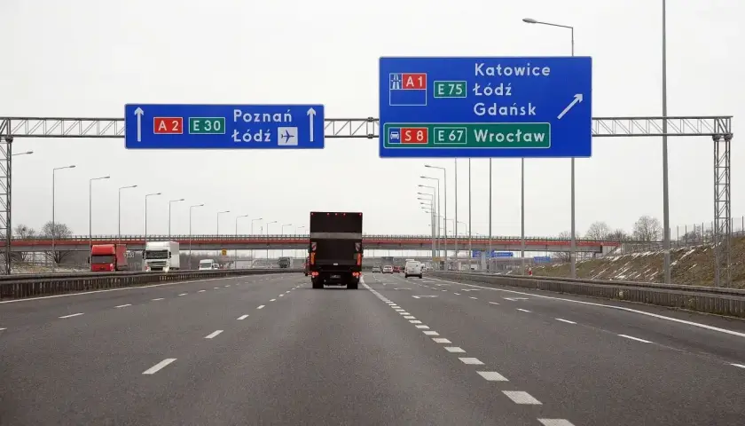 Autostrada z niebieskimi znakami drogowymi wskazującymi kierunki: Poznań, Łódź, Katowice, Gdańsk, Wrocław.