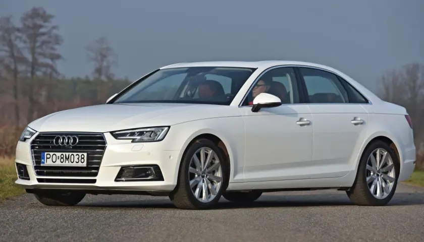 Białe Audi A4 sedan z kierowcą za kierownicą, zaparkowane na drodze.