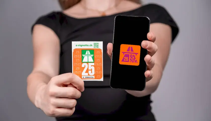 Kobieta pokazuje naklejkę i ekran telefonu z symbolem autostrady, symbolizującym winietę szwajcaria.