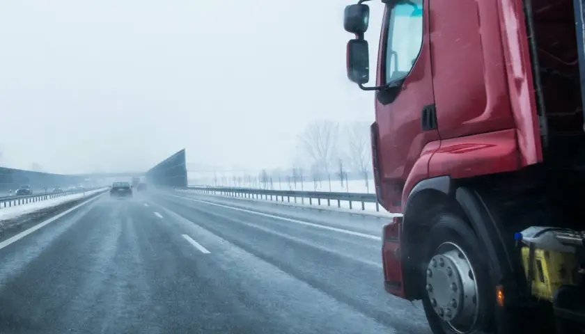 Czerwona ciężarówka na mokrej autostradzie w zimowy dzień. Kierowca zastanawia się, ile zarabia na godzinę, pokonując kolejne kilometry.