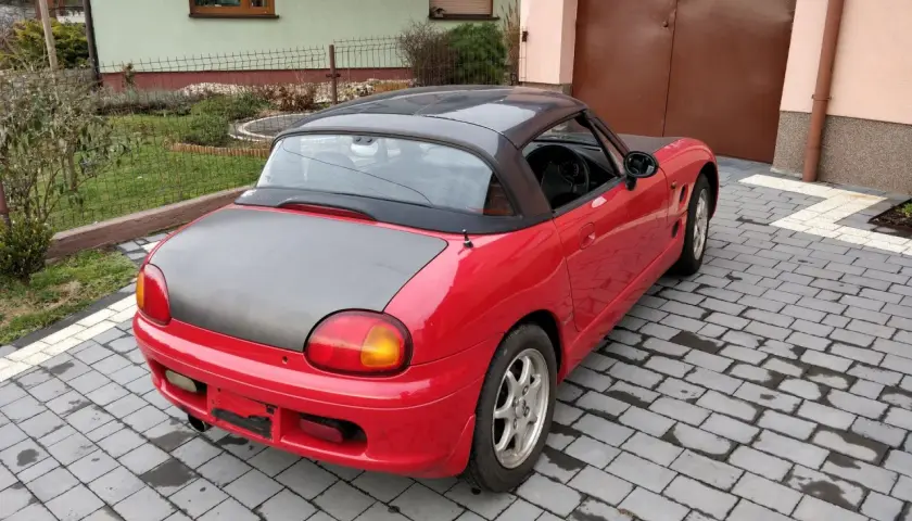 Czerwone Suzuki Cappuccino z czarnym dachem i maską stoi na podjeździe z kostki brukowej.