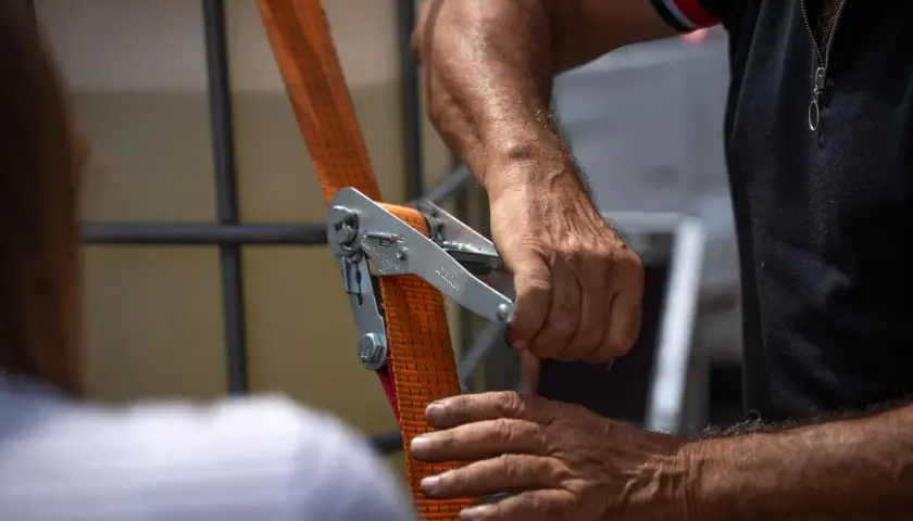 Dłonie mężczyzny obsługujące mechanizm napinający pomarańczową taśmę.