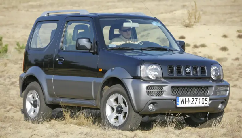 Czarny Suzuki Jimny na piasku. Kierowca w okularach. Pojemność baku tego modelu jest idealna na długie wyprawy.