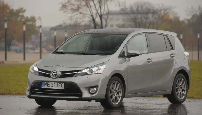 Srebrny minivan Toyota Verso zaparkowany na mokrej nawierzchni w deszczowy dzień.