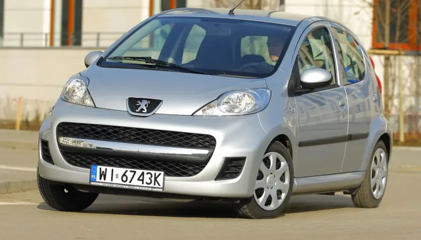 Srebrny Peugeot 107 z przodu, widoczny kierowca.
