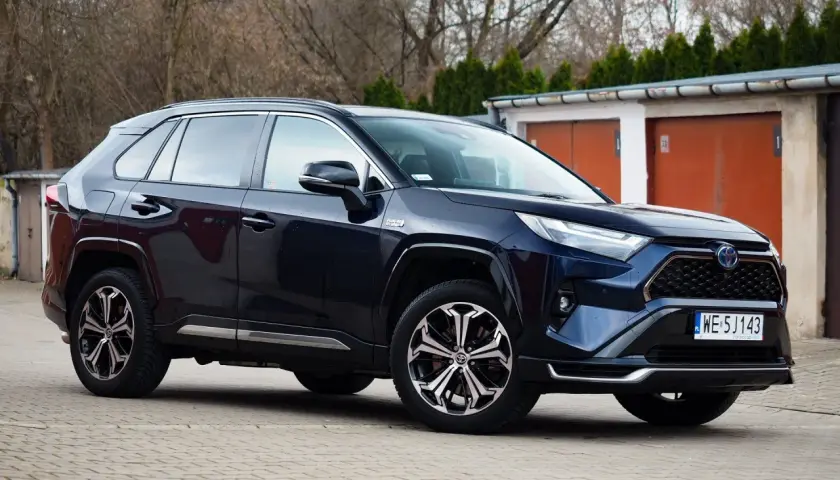 Ciemnoniebieski SUV Toyota RAV4 hybrydowy zaparkowany przed garażami.