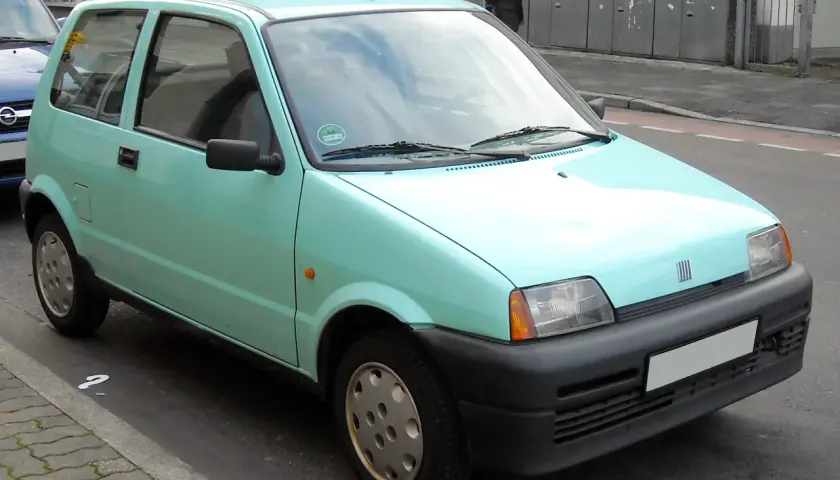 Jasnozielony Fiat Cinquecento zaparkowany na ulicy.
