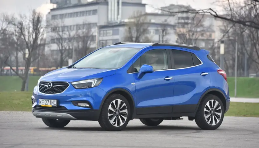 Niebieski Opel Mokka stoi na drodze, w tle budynki i drzewa.