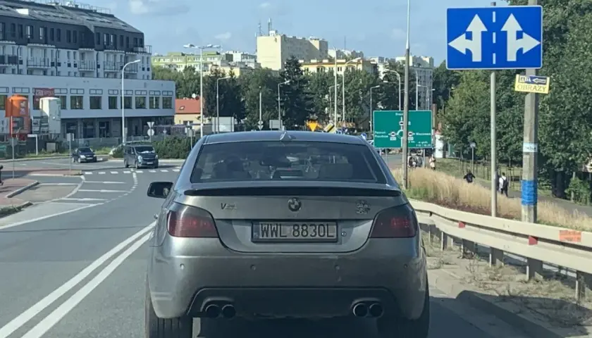 Szare BMW z rejestracją WWL 8830L na drodze, w tle budynki i znaki drogowe.