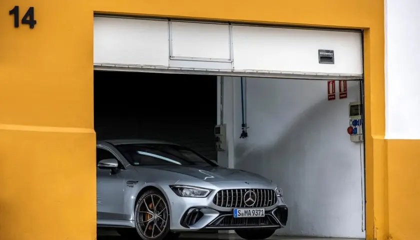 Srebrne coupe auto AMG GT 4-drzwiowe z brązowymi felgami stoi w garażu z żółtą ścianą.