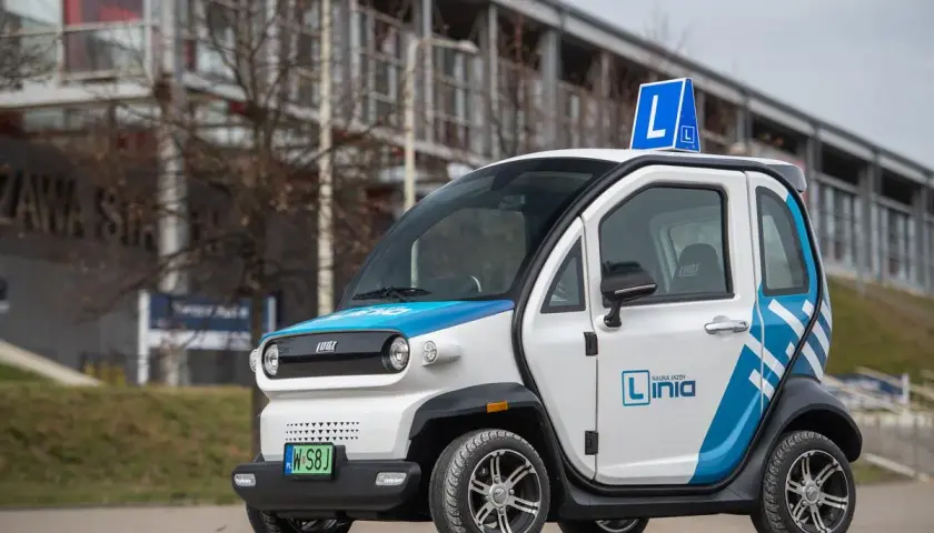 Mały, biało-niebieski pojazd samochodowy inny niż typowe auto, z literą "L" na dachu, idealny do nauki jazdy.