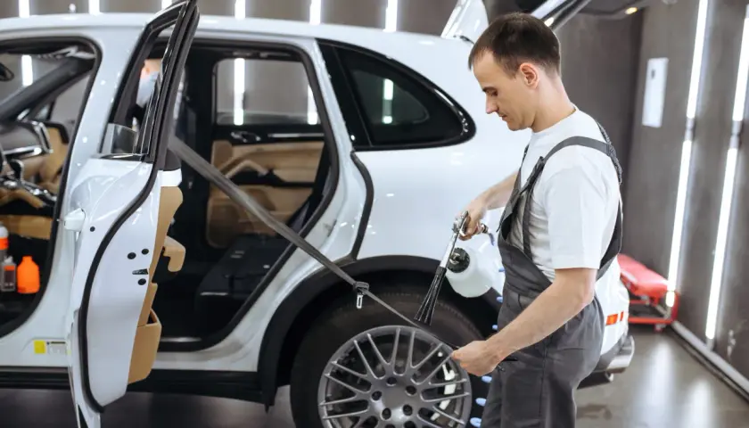 Pracownik detailingu samochodowego pokazuje, jak prać pasy bezpieczeństwa w białym SUV-ie, używając specjalistycznego sprzętu.