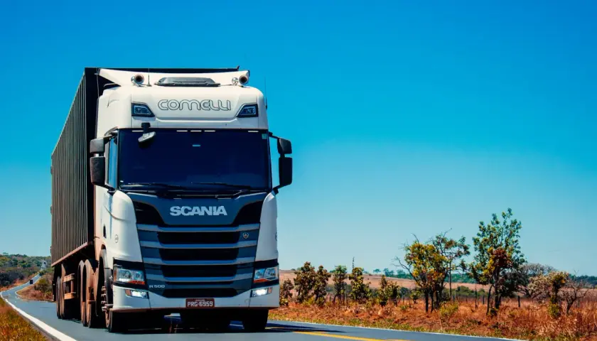 Biała ciężarówka Scania z naczepą jedzie po pustej drodze. Kierowca c. zarabia na życie, przewożąc towary.