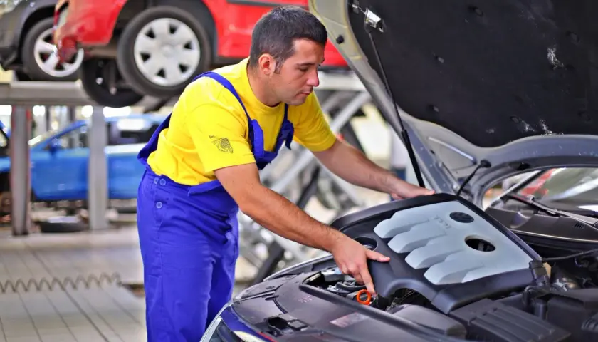 Mechanik w żółtej koszulce i niebieskich ogrodniczkach sprawdza silnik. Zastanawiasz się, ile zarabia kierowca mechanik?