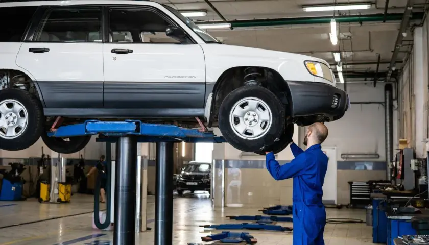 Mechanik w niebieskim kombinezonie naprawia podniesiony samochód, być może usuwając przyczynę piszczących hamulców.