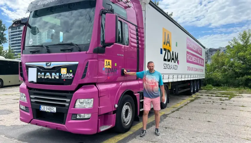 Mężczyzna obok różowej ciężarówki MAN, gotowy na zdobycie prawa jazdy kat C. Szkoła jazdy "Ja Zdam" zaprasza na kursy.