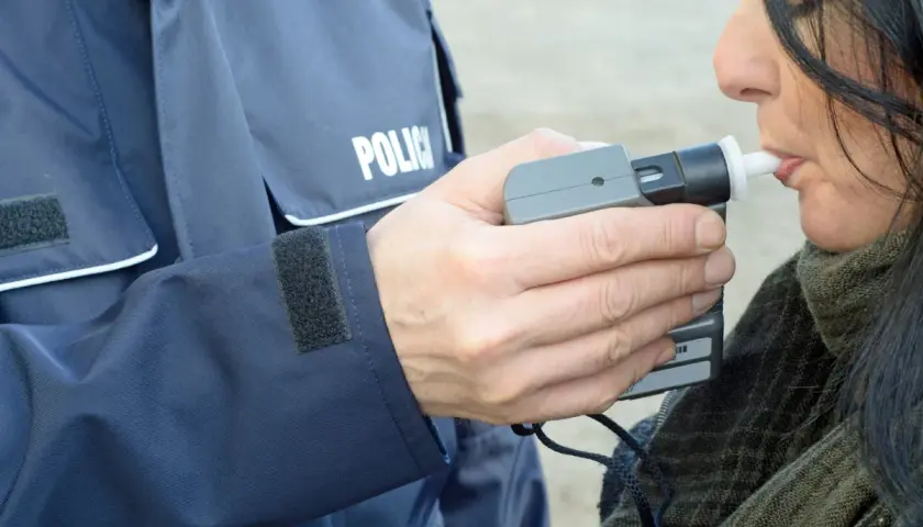 Policjant w mundurze z napisem "POLICJA" trzyma alkomat, a kobieta dmucha w jego ustnik. To przykład, jak dmuchać w alkomat.