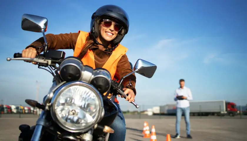 Uśmiechnięta kursantka na motorze, w kamizelce odblaskowej i kasku, uczy się jeździć. Zastanawiasz się, ile kosztuje prawo jazdy na motor?