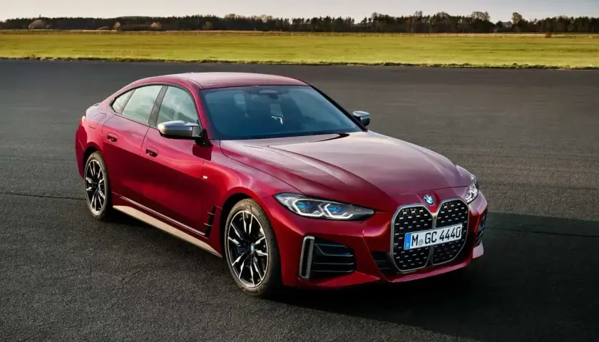 Czerwone BMW Gran Coupe na tle zielonych pól i błękitnego nieba. Elegancka linia nadwozia i sportowe felgi podkreślają dynamiczny charakter tego auta.
