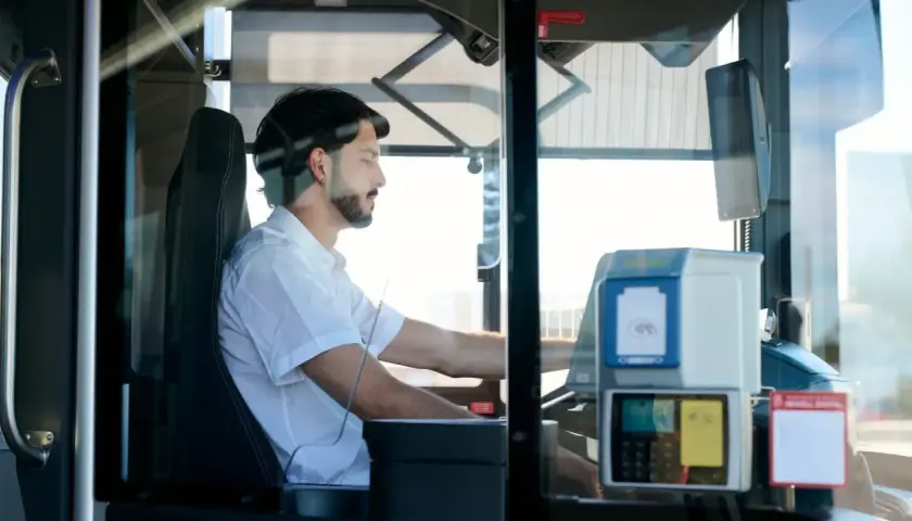 Mężczyzna za kierownicą autobusu, zastanawiający się, ile zarabia kierowca autobusu. Widoczny biletomat i siedzenie kierowcy.