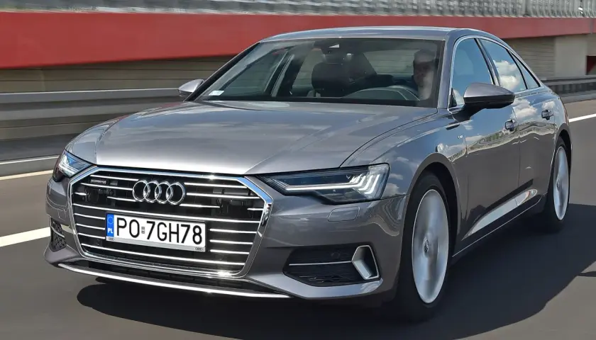 Szary sedan Audi A6 jedzie po drodze, widoczny przód i bok.
