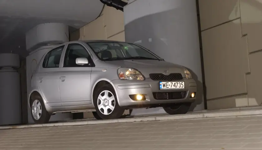 Srebrny Toyota Yaris 1.4 D4D, z tablicą WE 74735, zaparkowany pod betonowym zadaszeniem.
