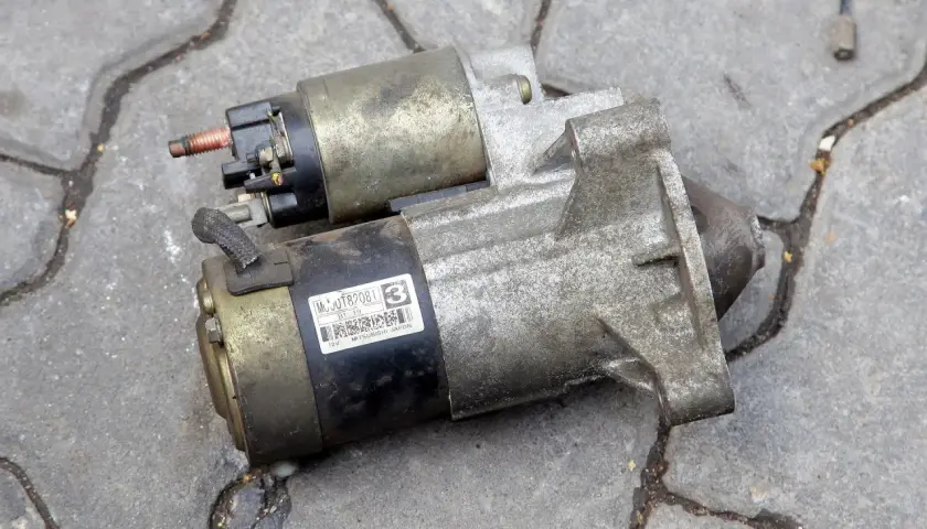 Rozrusznik samochodowy, kluczowy element do uruchomienia silnika. Widać jego metalową obudowę i złącza.