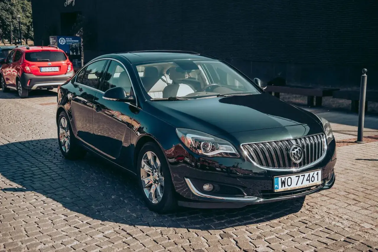 Elegancki, ciemnozielony Buick Regal z chromowanymi felgami stoi na brukowanej ulicy.