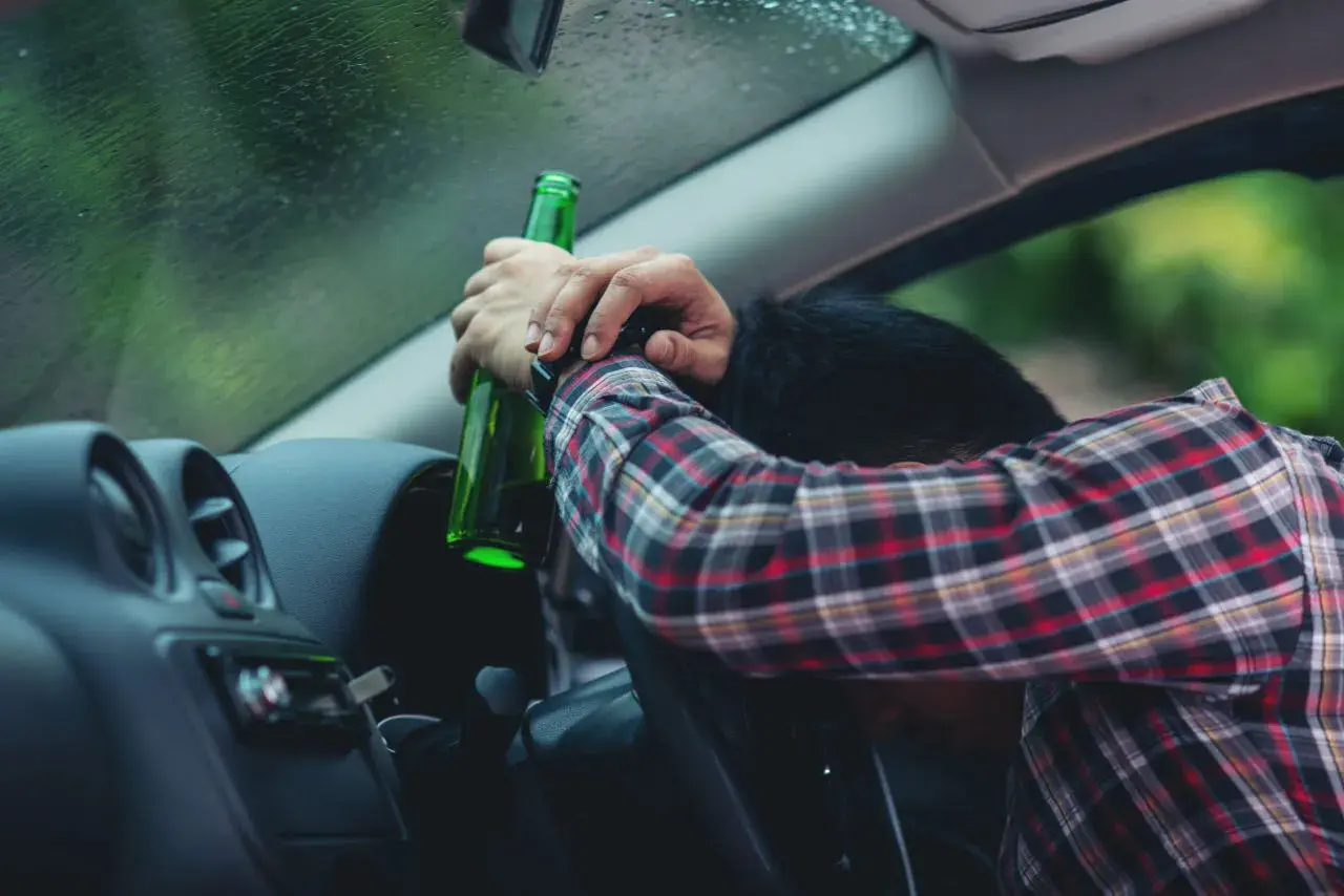Pijany kierowca z butelką piwa w ręku. Za alkohol 1 promil prawo jazdy zabierają.
