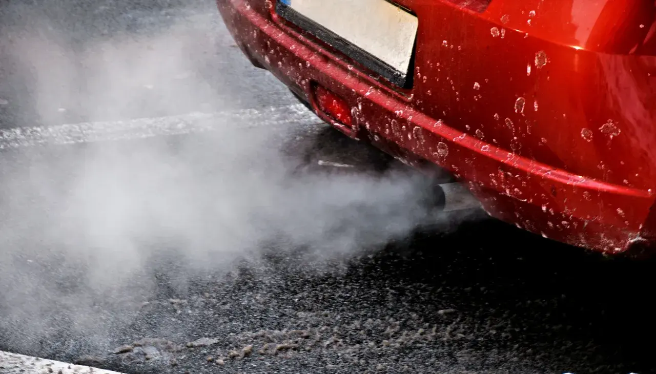 Z rury wydechowej czerwonego auta wydobywa się biały dym, jakby rozbiegany diesel próbował złapać oddech.
