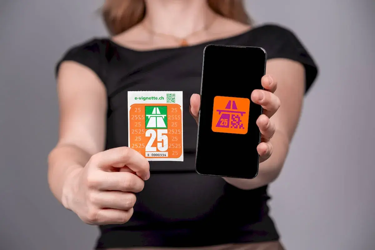 Kobieta pokazuje naklejkę i ekran telefonu z symbolem autostrady, symbolizującym winietę szwajcaria.