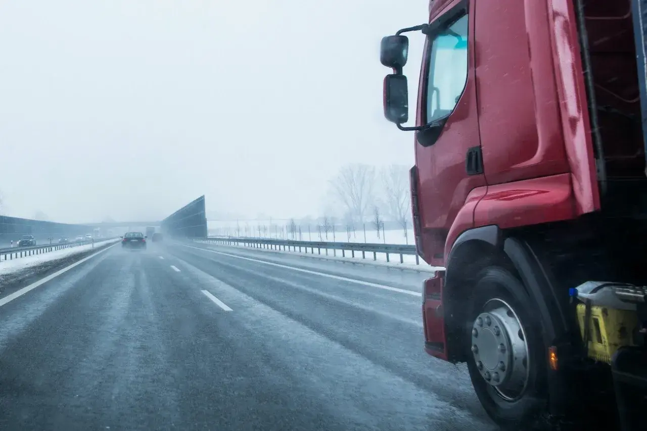 Czerwona ciężarówka na mokrej autostradzie w zimowy dzień. Kierowca zastanawia się, ile zarabia na godzinę, pokonując kolejne kilometry.