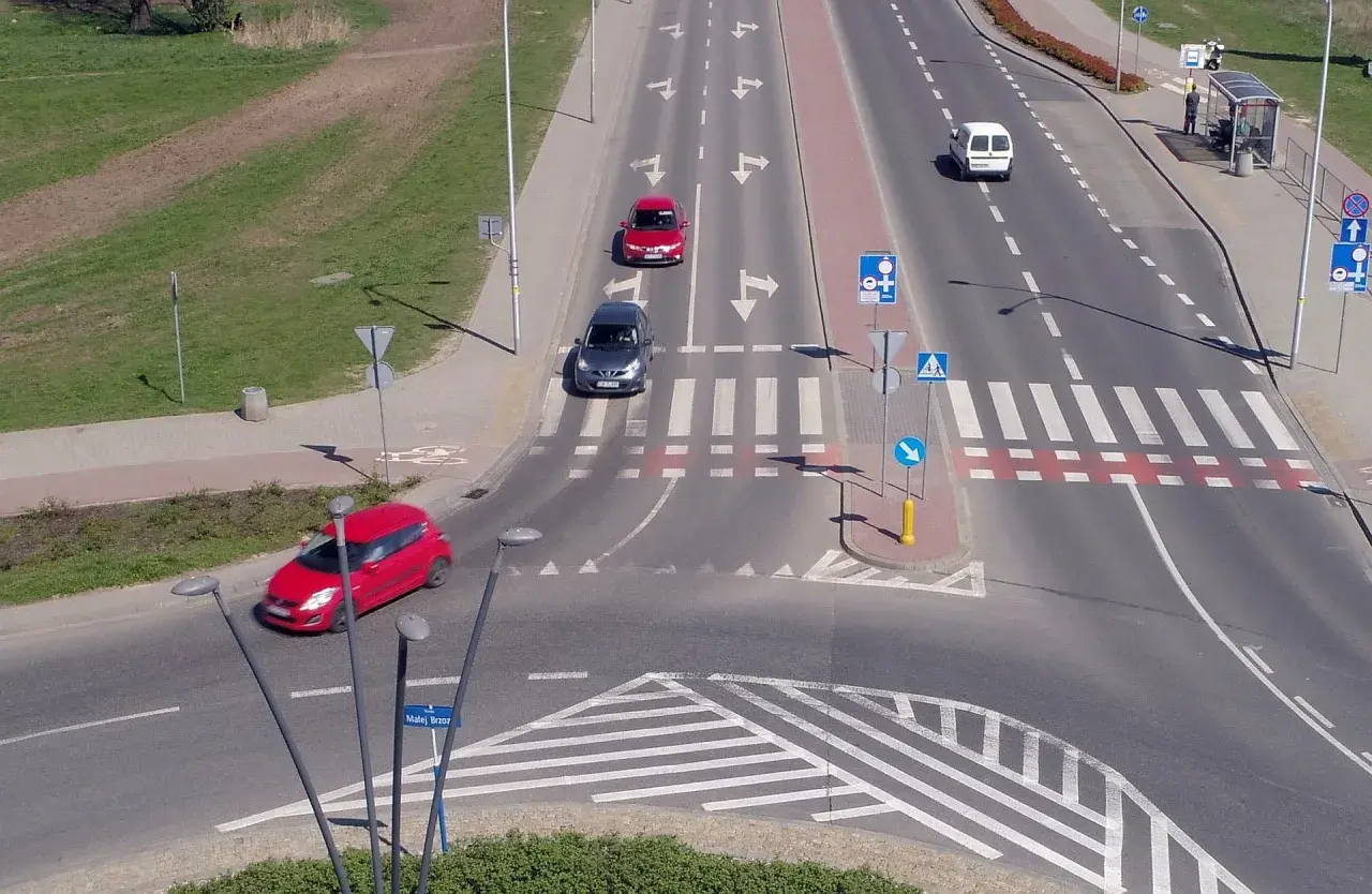 Samochody poruszają się po skrzyżowaniu z oznakowaniem sugerującym rondo turbinowe.