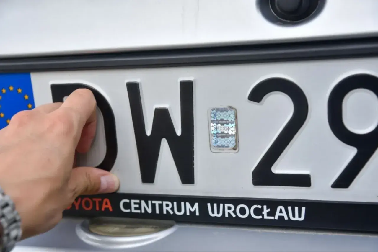 Dłoń poprawia hologram na tablicy rejestracyjnej DW 29. Toyota Centrum Wrocław.