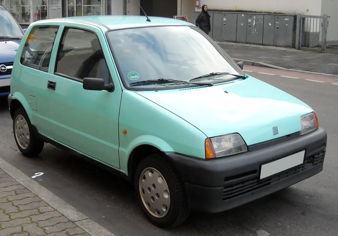 Jasnozielony Fiat Cinquecento zaparkowany na ulicy.