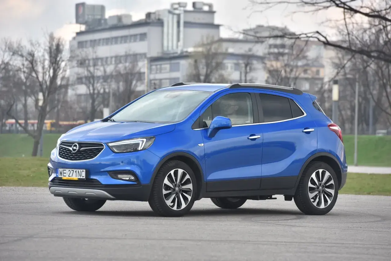 Niebieski Opel Mokka stoi na drodze, w tle budynki i drzewa.