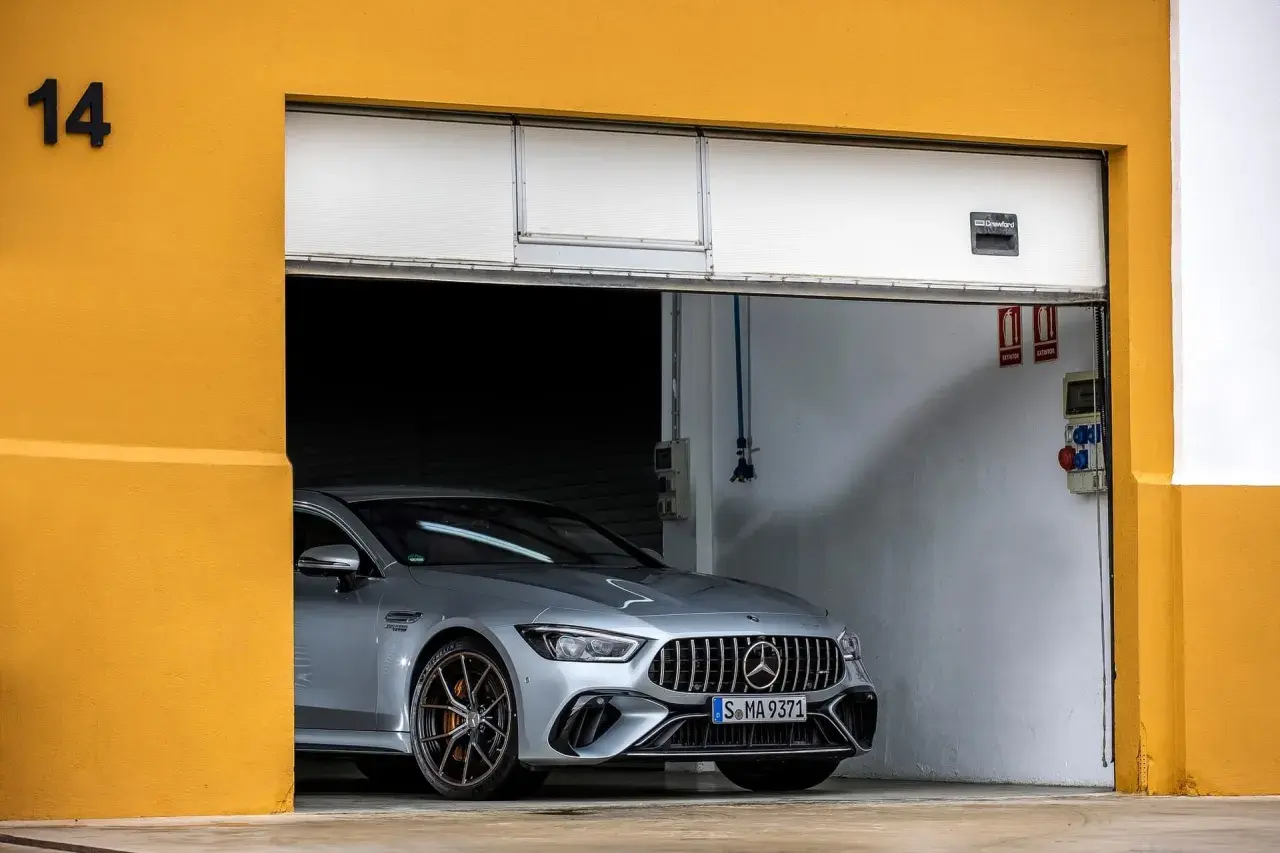 Srebrne coupe auto AMG GT 4-drzwiowe z brązowymi felgami stoi w garażu z żółtą ścianą.